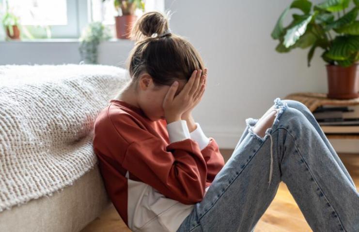 Nuori tyttö kädet silmillään istuu lattialla